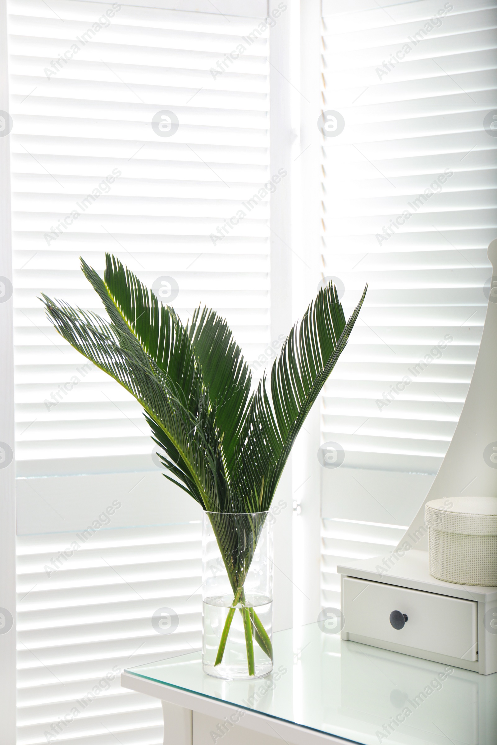 Photo of Green tropical leaves in vase on table. Modern decor for stylish interior