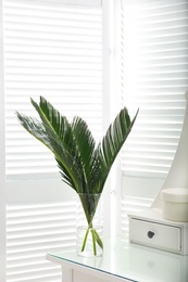 Photo of Green tropical leaves in vase on table. Modern decor for stylish interior