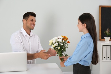 Schoolgirl congratulating her pedagogue with bouquet in classroom. Teacher's day