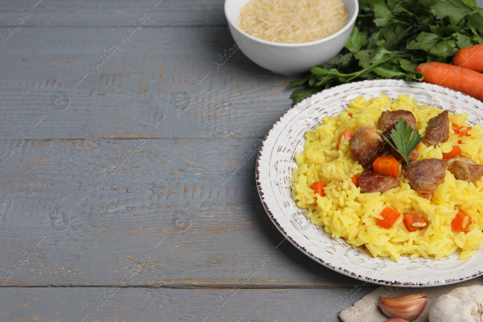 Photo of Delicious pilaf with meat and ingredients on grey wooden table. Space for text