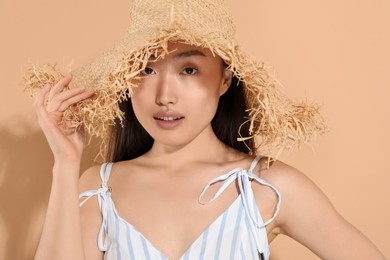 Beautiful young woman in straw hat on beige background