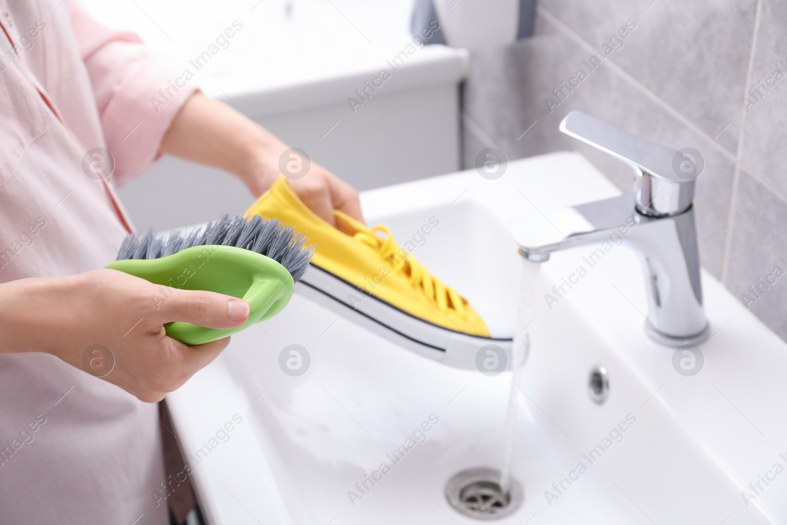 Photo of Woman washing stylish sneakers with brush in sink, closeup