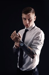Photo of Young man with tattoos and wristwatch on black background
