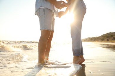 Photo of Couple on sandy beach near sea at sunset, closeup of legs