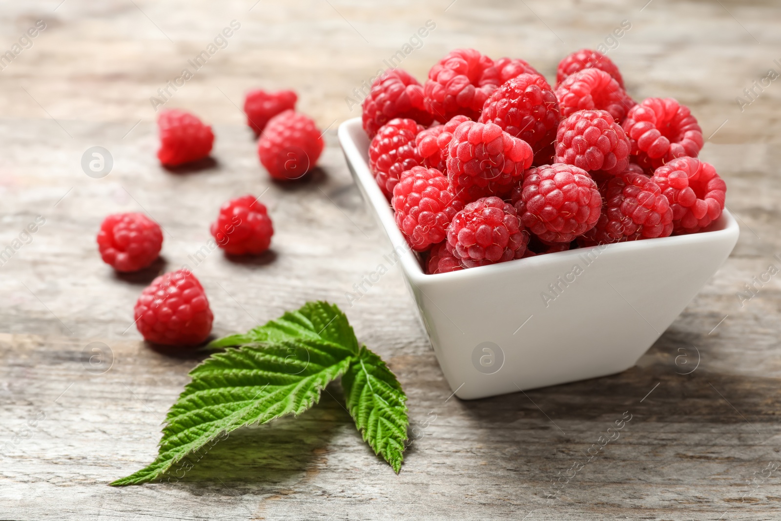 Photo of Bowl with ripe aromatic raspberries on wooden table