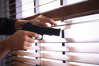 Man aiming through window blinds indoors, closeup