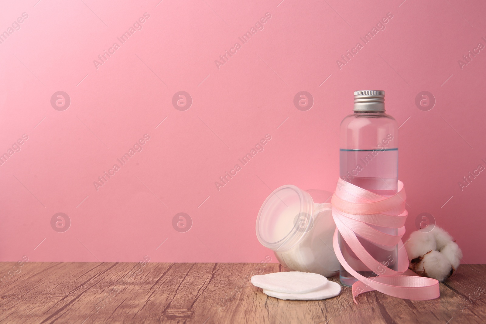 Photo of Composition with makeup remover and cotton flower on wooden table against pink background, space for text