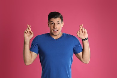 Photo of Man with crossed fingers on pink background. Superstition concept