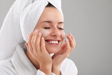 Photo of Woman applying cosmetic product onto her face against grey background, space for text. Spa treatments