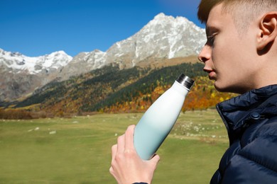 Photo of Boy drinking from thermo bottle in mountains on sunny day. Space for text