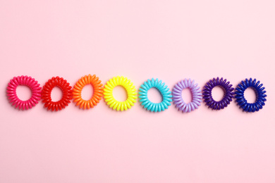 Colorful spiral rubber bands on pink background, flat lay