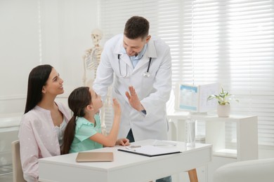 Photo of Mother with daughter visiting pediatrician in hospital. Doctor giving high five to little girl