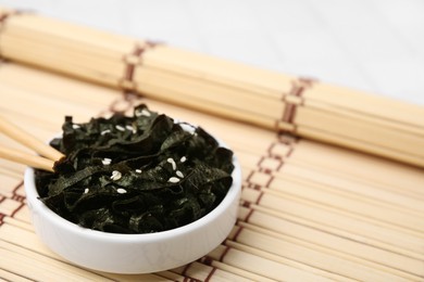 Photo of Chopped nori sheets with sesame and chopsticks on bamboo mat, closeup. Space for text