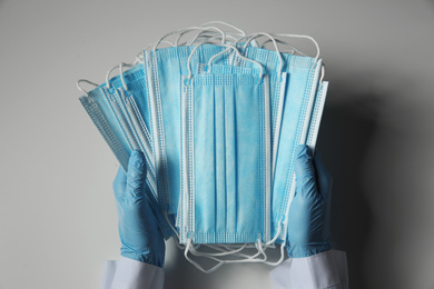 Photo of Doctor in latex gloves holding disposable face masks on light background, closeup. Protective measures during coronavirus quarantine