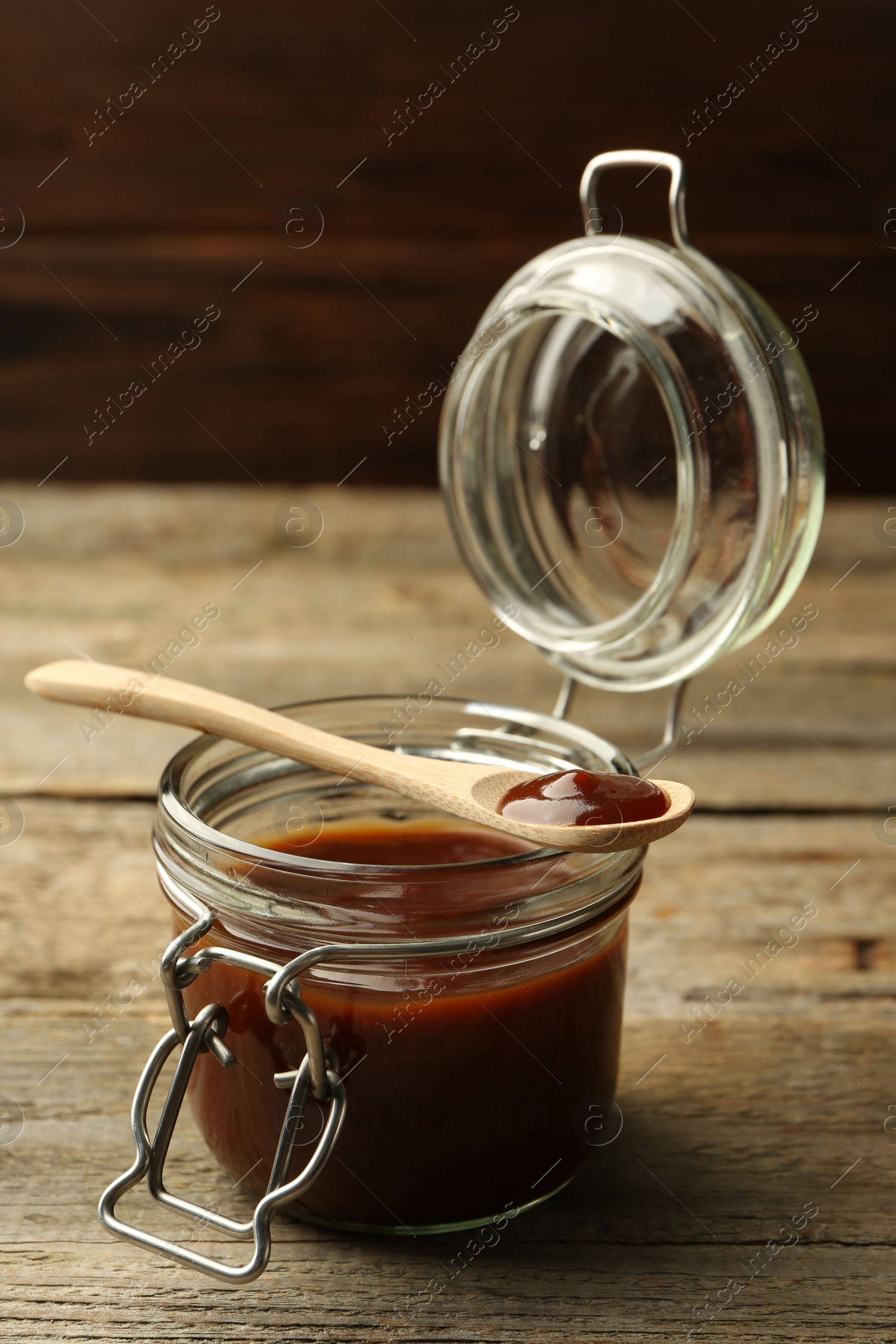 Photo of Tasty barbeque sauce in jar and spoon on wooden table