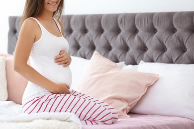 Happy pregnant woman sitting on bed at home, closeup