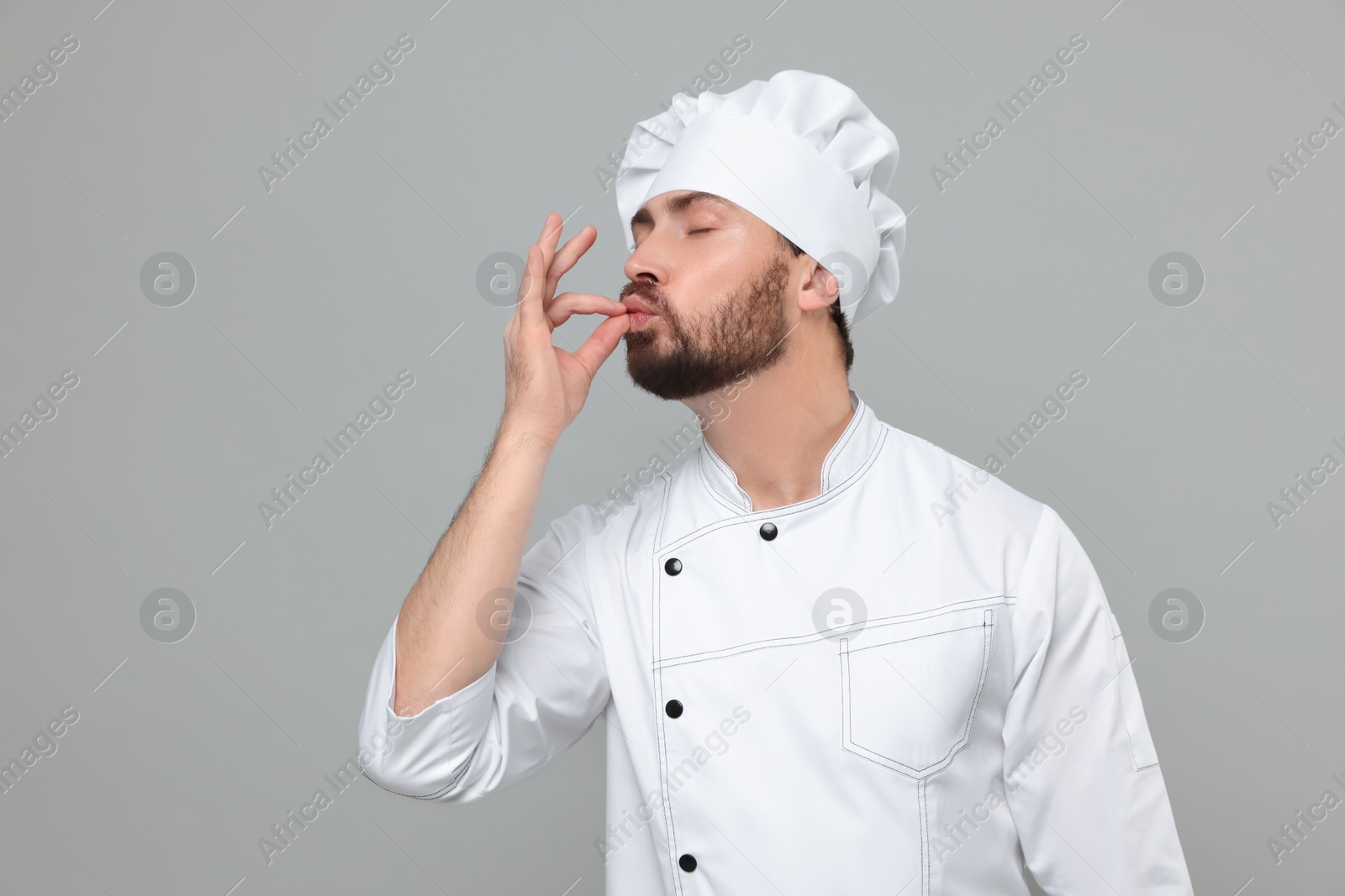 Photo of Mature chef showing delicious gesture on grey background, space for text