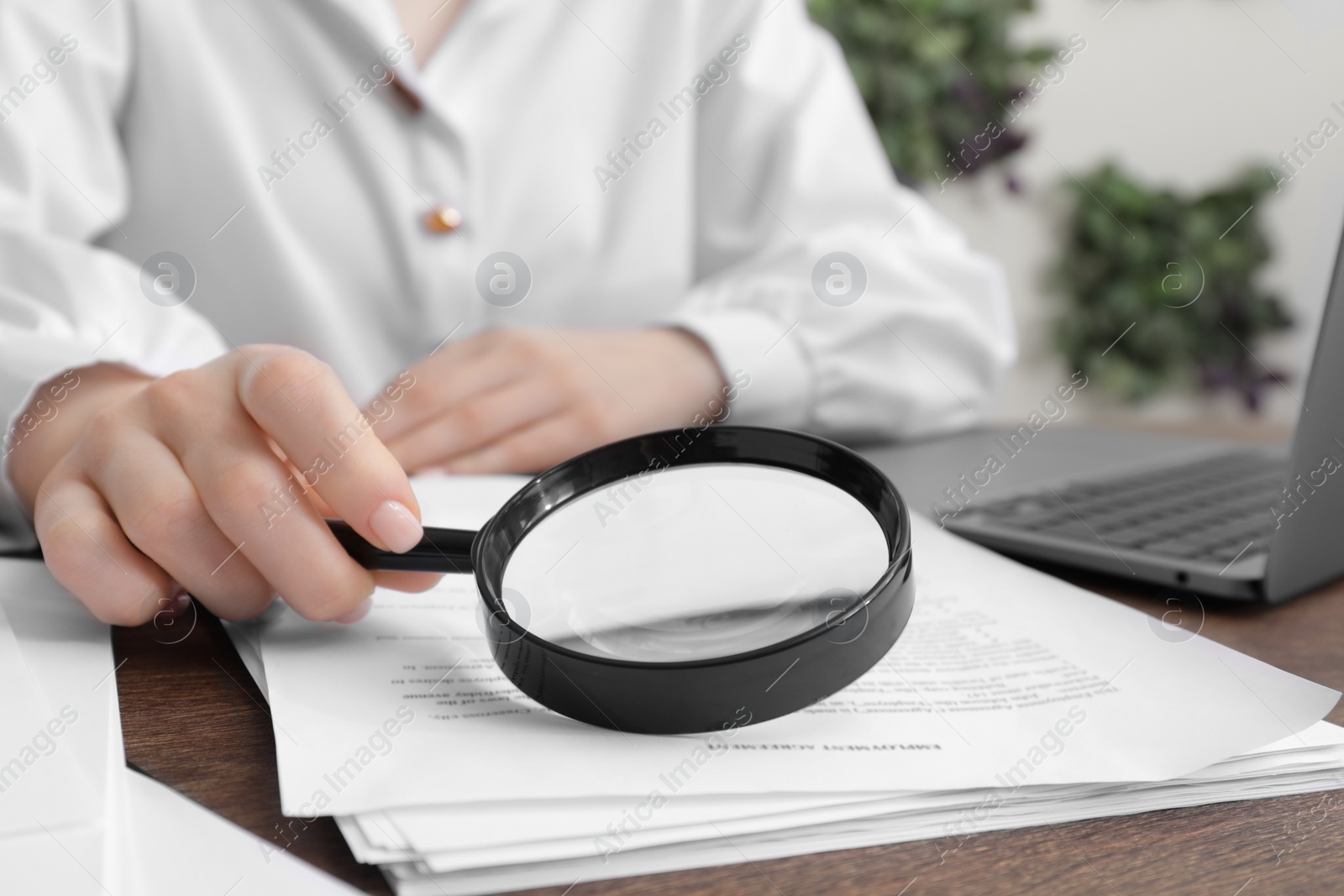 Photo of Woman looking at document through magnifier at wooden table indoors, closeup. Searching concept