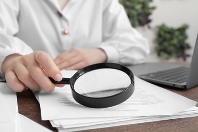 Photo of Woman looking at document through magnifier at wooden table indoors, closeup. Searching concept