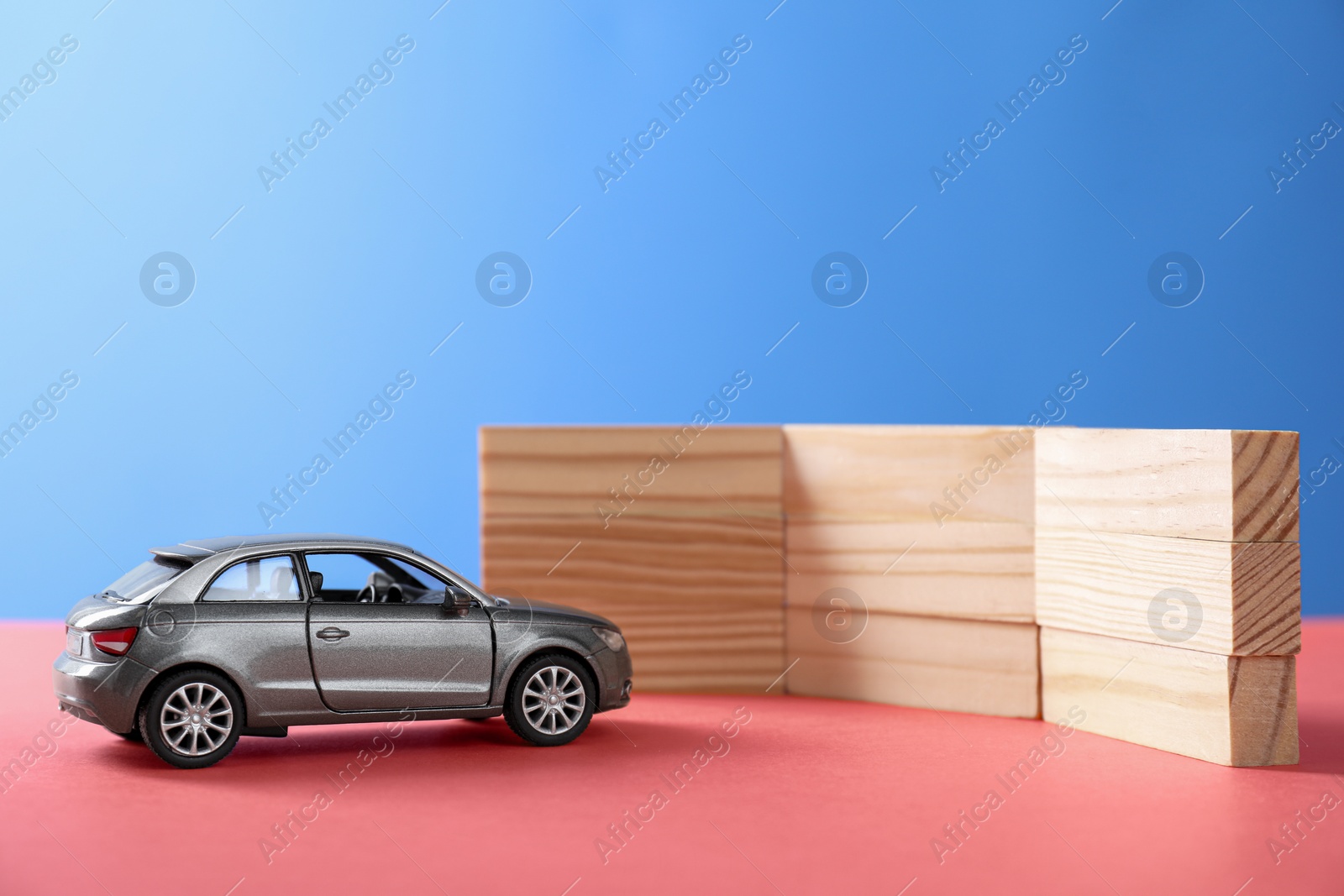 Photo of Development through barriers overcoming. Silver toy car movement blocked by wooden blocks on coral surface, space for text