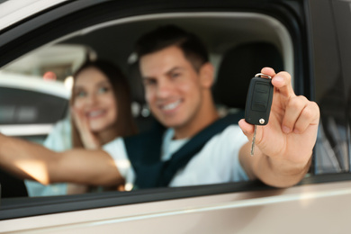 Photo of Happy couple sitting in modern car at dealership, focus on hand with key