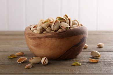 Photo of Tasty pistachios in bowl on wooden table, closeup