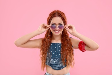 Photo of Stylish young hippie woman in sunglasses on pink background