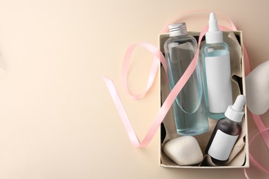Bottles of cosmetic products in box, stones and ribbon on beige background, top view. Space for text