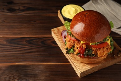 Photo of Delicious burger with crispy chicken patty and sauce on wooden table. Space for text