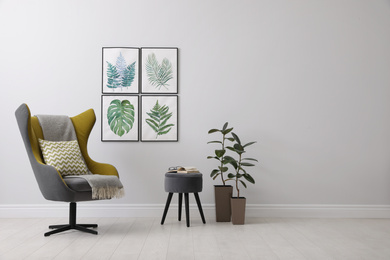 Photo of Stylish room interior with comfortable armchair and paintings of tropical leaves. Space for text