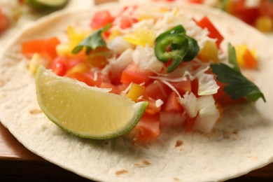 Delicious taco with vegetables, lime and parsley on table, closeup