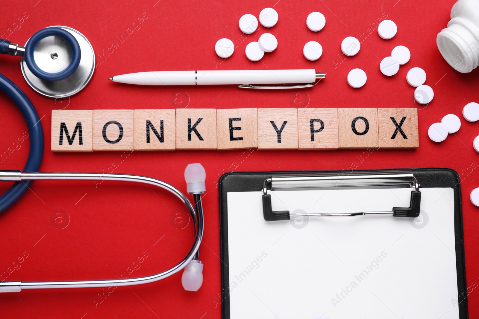Photo of Word Monkeypox made of wooden cubes, pills and stethoscope on red background, flat lay