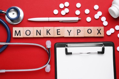 Photo of Word Monkeypox made of wooden cubes, pills and stethoscope on red background, flat lay