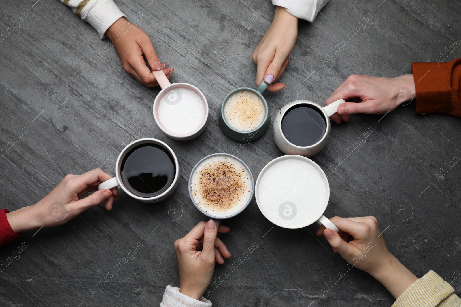 Photo of People holding different cups with aromatic hot coffee at grey table, top view