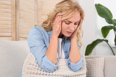 Photo of Woman suffering from headache on sofa at home. Hormonal disorders