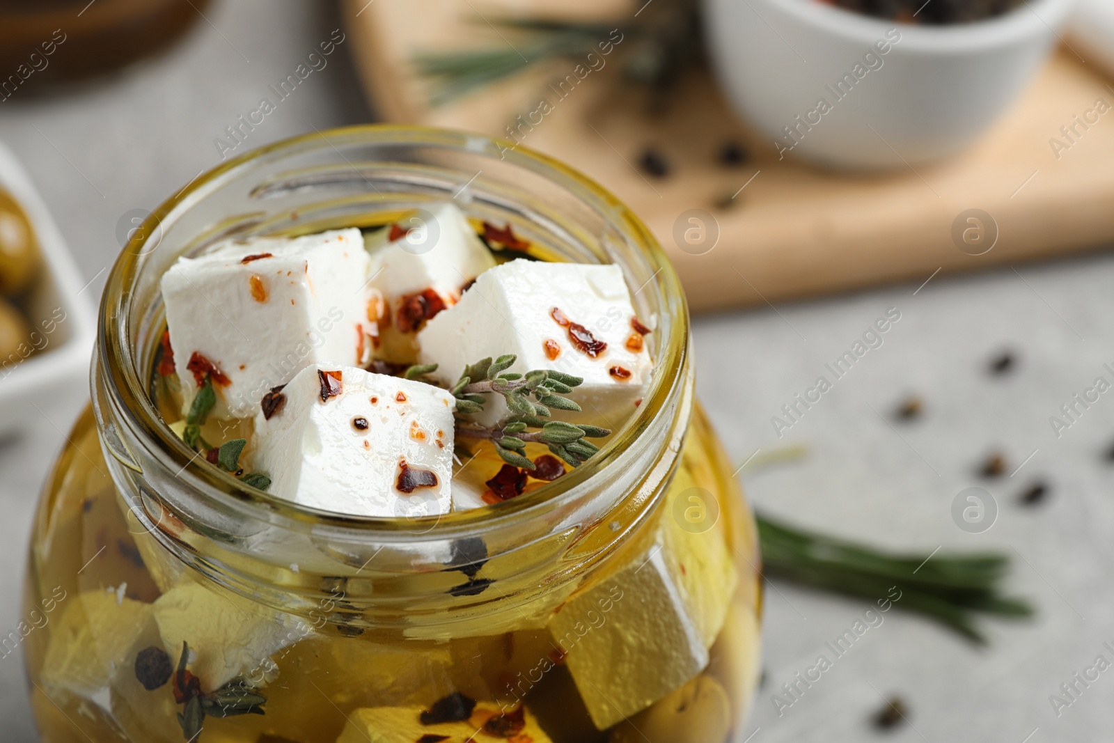 Photo of Jar with feta cheese marinated in oil on light grey table, closeup. Pickled food