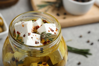 Photo of Jar with feta cheese marinated in oil on light grey table, closeup. Pickled food