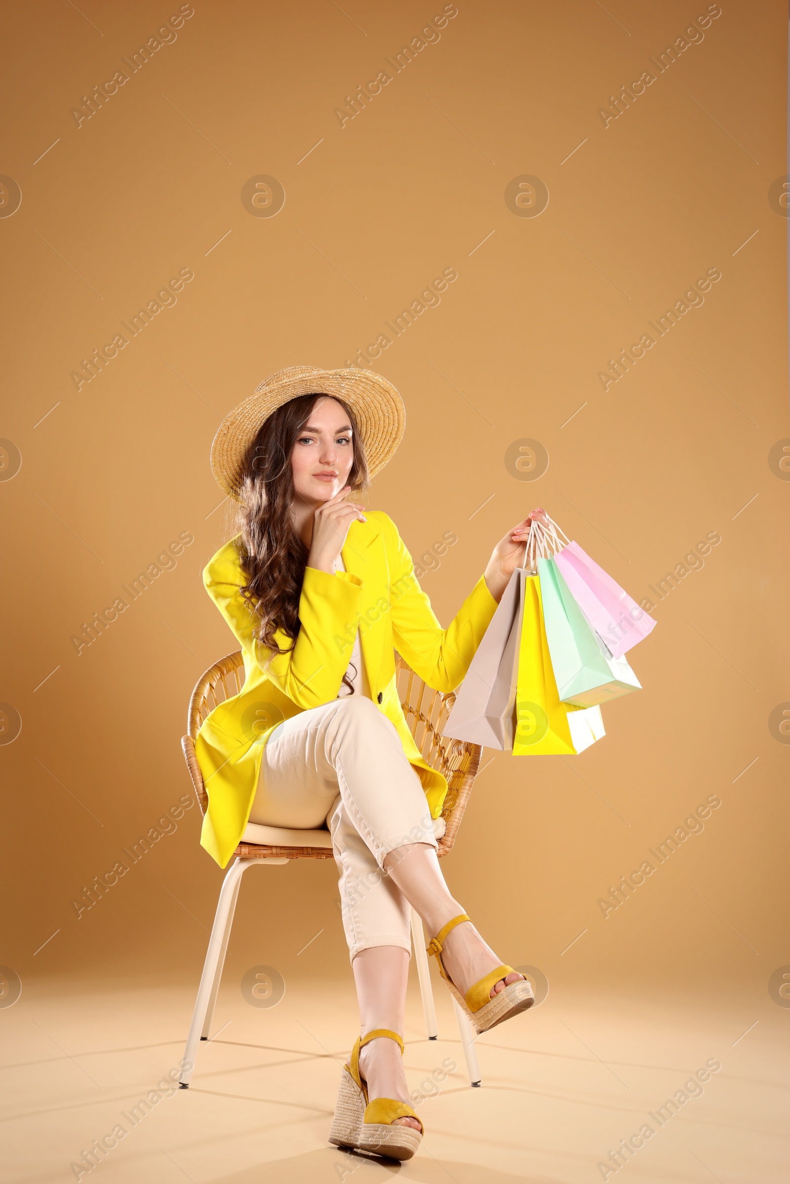 Photo of Young woman holding many colorful shopping bags on armchair against beige background