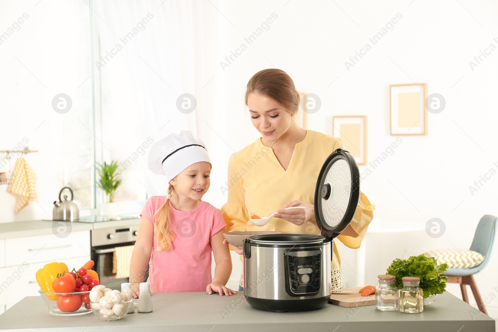 Photo of Mother and daughter preparing food with modern multi cooker in kitchen