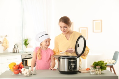 Photo of Mother and daughter preparing food with modern multi cooker in kitchen