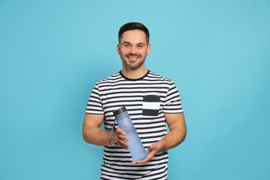 Happy man holding transparent plastic bottle of water on light blue background