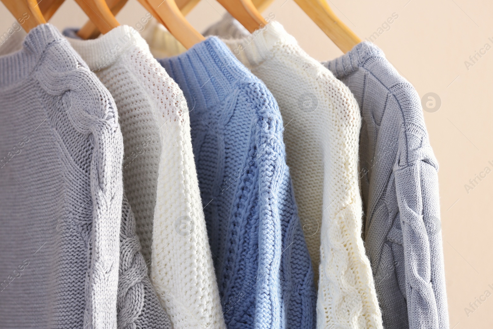 Photo of Collection of warm sweaters hanging on rack near light wall, closeup