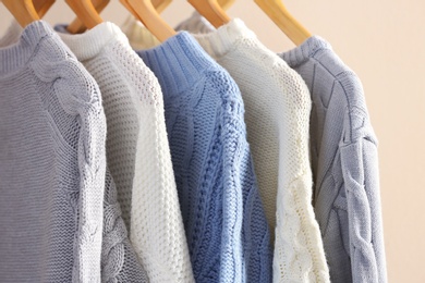 Photo of Collection of warm sweaters hanging on rack near light wall, closeup