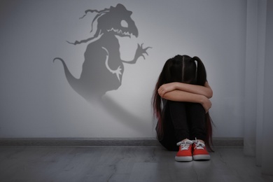 Image of Shadow of monster on wall and scared little girl in room