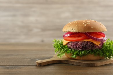 Photo of Tasty vegetarian burger with beet patty on wooden table. Space for text