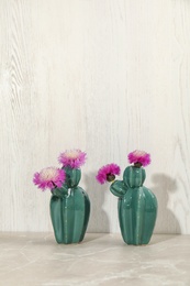 Trendy cactus shaped ceramic vases with flowers on table against wooden background
