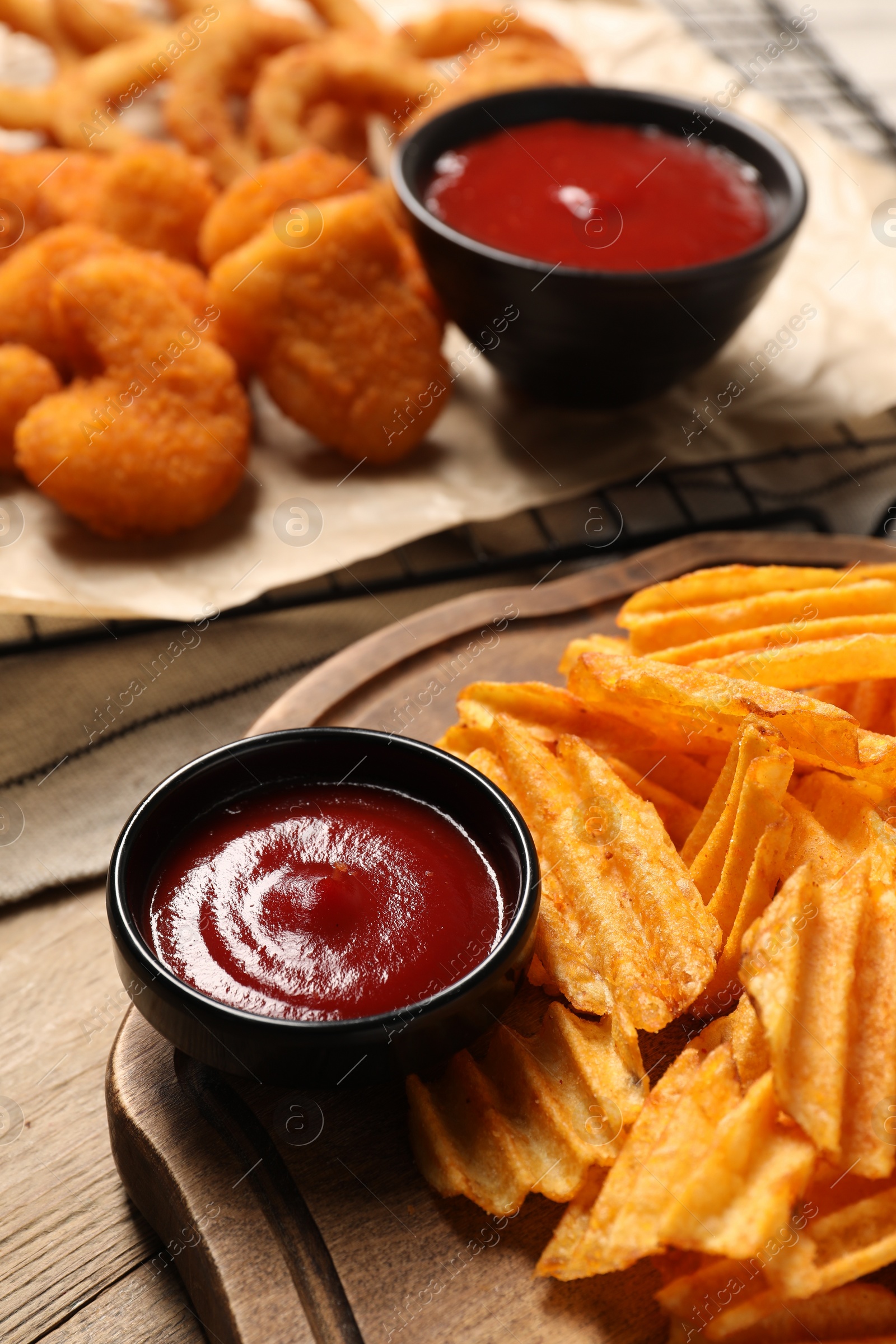 Photo of Tasty ketchup and snacks on wooden table, selective focus