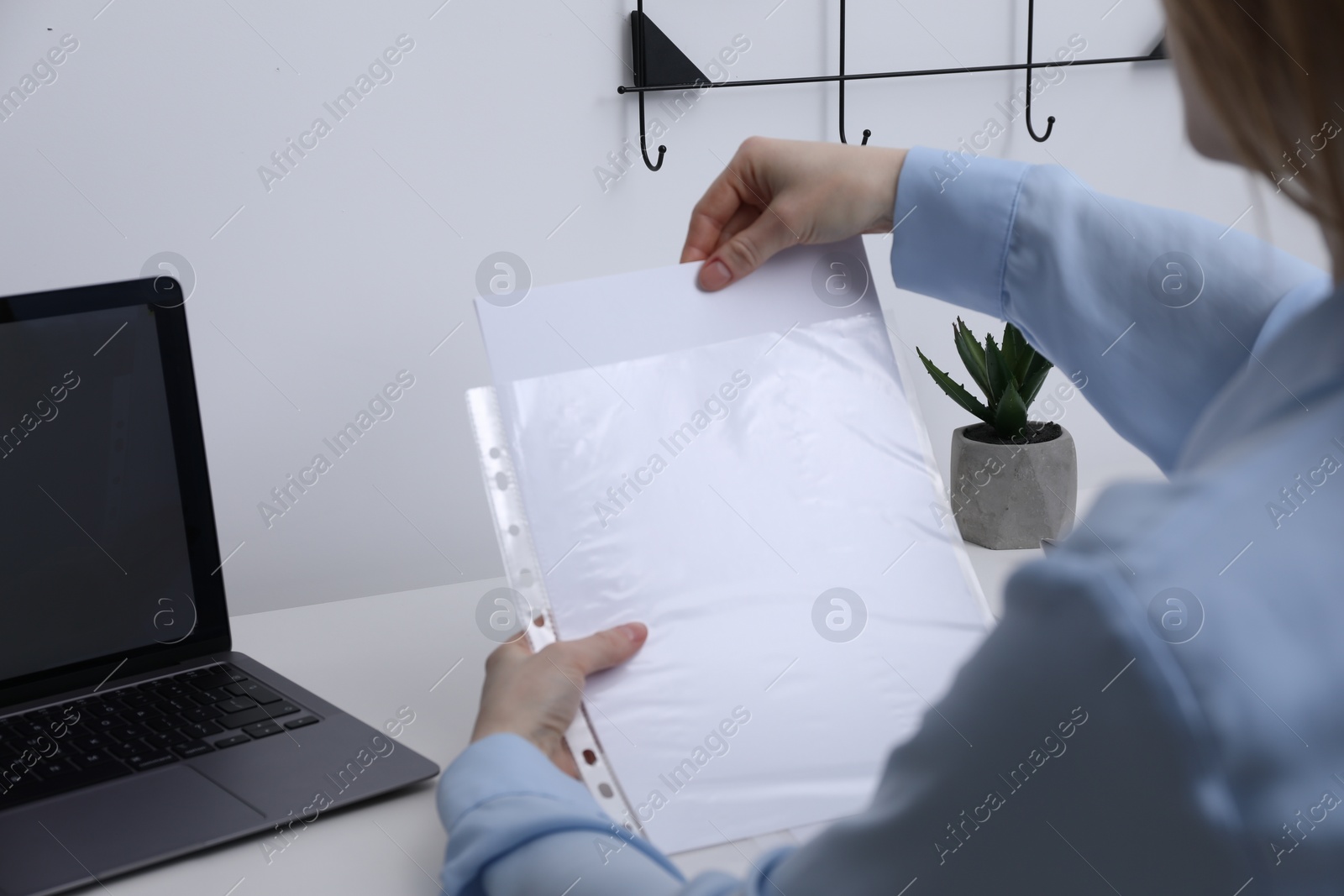 Photo of Woman putting paper sheet into punched pocket at table, closeup