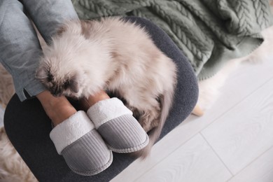 Photo of Woman in stylish soft slippers resting with cute cat at home, top view