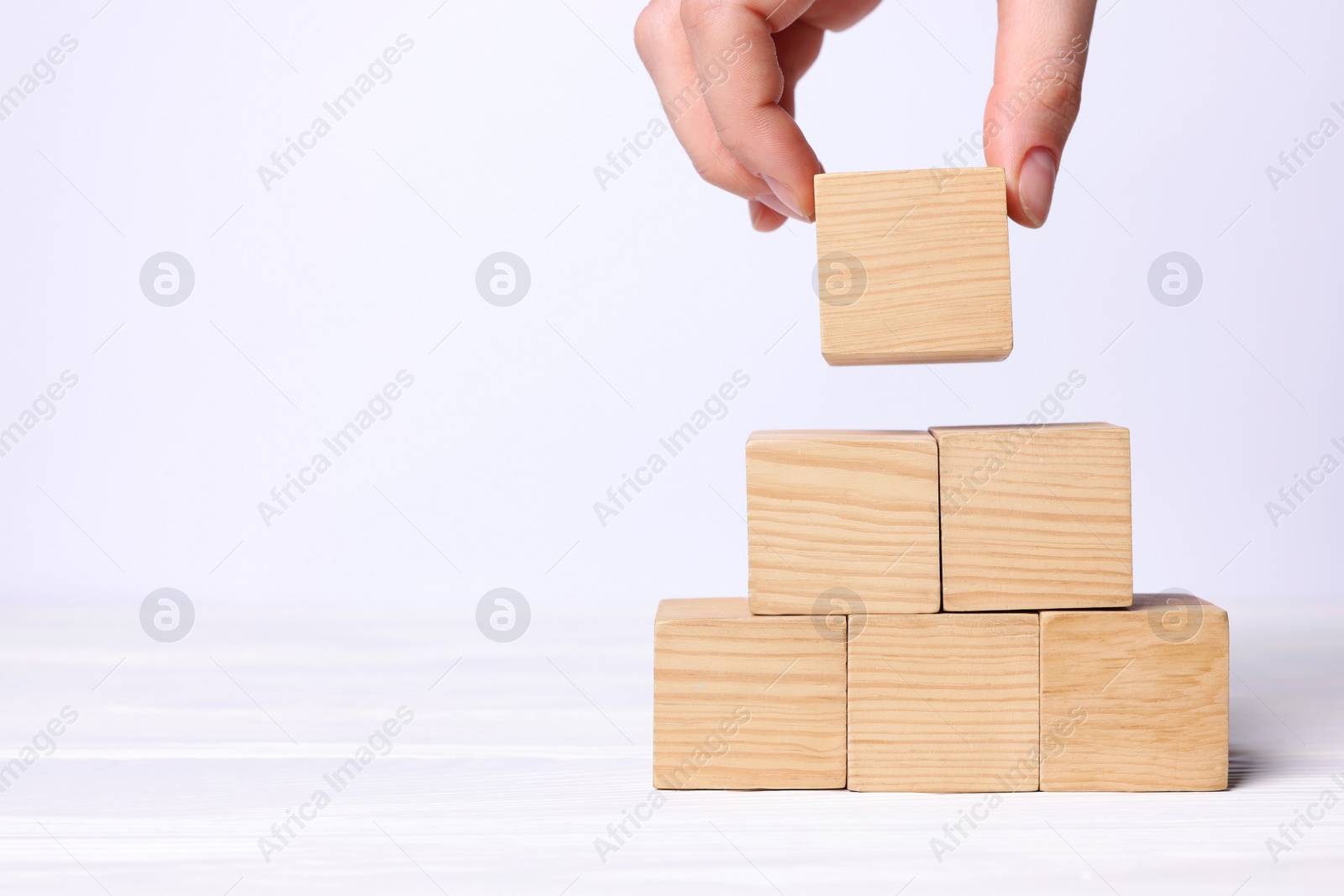 Photo of Woman building pyramid of cubes on white background, closeup with space for text. Idea concept